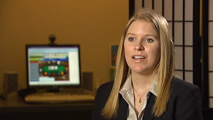 Foto di un’autrice bionda con giacca scura, seduta in ufficio davanti a uno schermo di computer